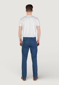 Pantaloni blu con una finitura liscia, vestibilità su misura e due tasche posteriori, abbinati a una maglietta bianca a maniche corte.