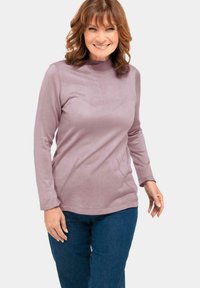 Hellblaues langärmeliges Oberteil mit einem Mock-Turtleneck, das diagonale Perforationen am Saum aufweist, kombiniert mit dunkelblauen Jeans.