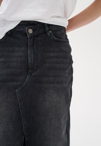 Black denim skirt with a front slit and vertical ribbed texture. Features a metal button closure and standard belt loops.