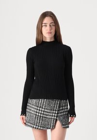 Pulover negru cu guler înalt și mâneci lungi, asortat cu o fustă în carouri alb-negru cu fante laterale și nasturi la manșete.