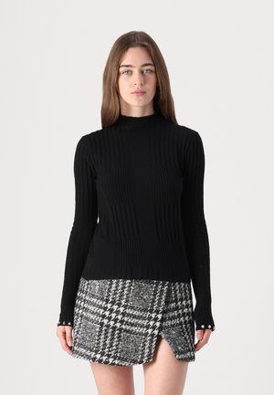 Maglione nero a costine con collo alto e maniche lunghe, abbinato a una gonna houndstooth bianca e nera con una fessura laterale e bottoni ai polsini.