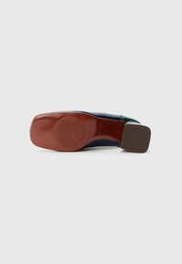 Scarpa con tacco dal morbido upper blu navy, dettagli verdi e suola in gomma marrone caratterizzata da un logo in rilievo circolare e scanalature orizzontali.
