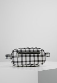 Sac à damier noir et blanc de forme rectangulaire, fabriqué en matériau texturé, avec une fermeture éclair à l'avant et une poignée latérale.