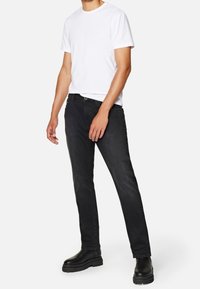 Jeans negros combinados con una camiseta blanca, con un corte recto, lazos para el cinturón y bolsillos laterales. Las botas son negras y tienen una suela texturizada.