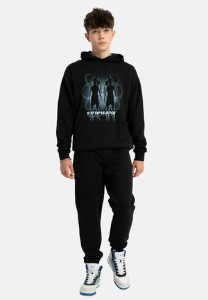 Czarna bluza z kapturem z graficznym nadrukiem sylwetek i napisem "EPIPHANY", zestawiona z czarnymi dresami i szarymi trampkami z niebieskimi akcentami.