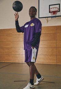 Canottiera da basket viola a maniche corte, sotto maglia nera, pantaloncini abbinati e una palla da basket. Sneakers bianche con accenti neri.