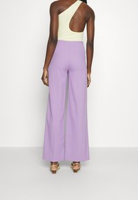 Lichtgroene geribde one-shoulder bodysuit, gecombineerd met hooggetailleerde lavendelkleurige wijde broek met een gladde stof en subtiele glans.