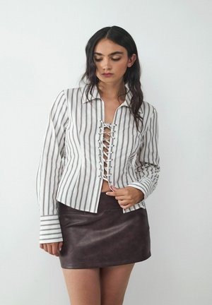 Weiß- und braun geringeltes Button-Up-Shirt mit einem Schnürdesign an der Vorderseite, kombiniert mit einem taillierten, dunkelbraunen Leder-Minirock.