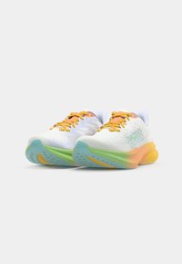 Baskets de sport blanches avec des lacets orange, dotées d'un dessus texturé et d'une semelle rembourrée avec des accents pastel verts, bleus et jaunes.