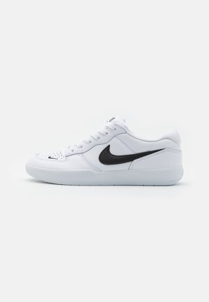 Adidași albi din piele cu o textură netedă. Prezintă logo-ul negru Nike pe lateral, vârf rotund și sistem de închidere cu șireturi. Talpă din cauciuc.