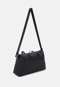 Sac de sport noir avec une surface en tissu lisse, une longue sangle réglable et des finitions en métal doré. Il dispose de deux poignées supérieures et d'une fermeture à glissière.