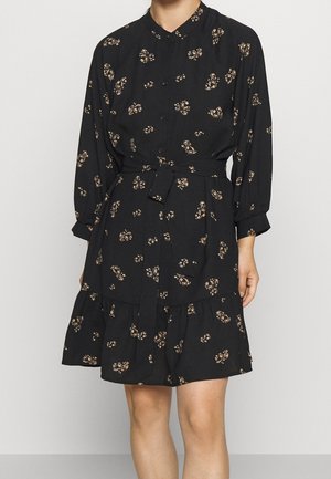 Robe noire boutonnée avec un col rond, motif floral dans des tons beiges, manches longues, taille ceinturée et ourlet volanté à étages.