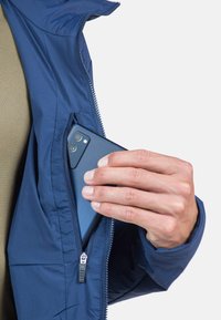 Marineblaues Jacket mit einer Reißverschlusstasche, die ein Smartphone hält. Der Stoff erscheint glatt und leicht, geeignet für aktive Freizeitgestaltung.