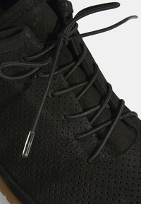 Zwarte geperforeerde schoen met een gladde textuur, ronde neus en zwarte veters. Voorzien van een transparante plastic veteraglet en rubberen zool.