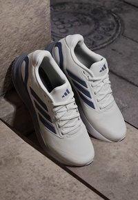 Weiße und marineblaue Sportschuhe mit Schnürsenkeln, auf Steinstufen und Betonpflaster platziert, seitlich nebeneinander angeordnet.