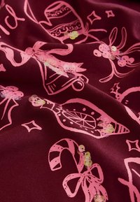 Burgundy tyg med en glänsande textur pryds av rosa festliga mönster, inklusive klockor, klubbor och rosetter, dekorerade med blanka paljetter.
