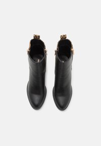 Botas de cuero negras hasta el tobillo con puntera afilada, forro de estampado de leopardo y herrajes de cremallera en tono dorado a los lados. Textura suave y diseño elegante.