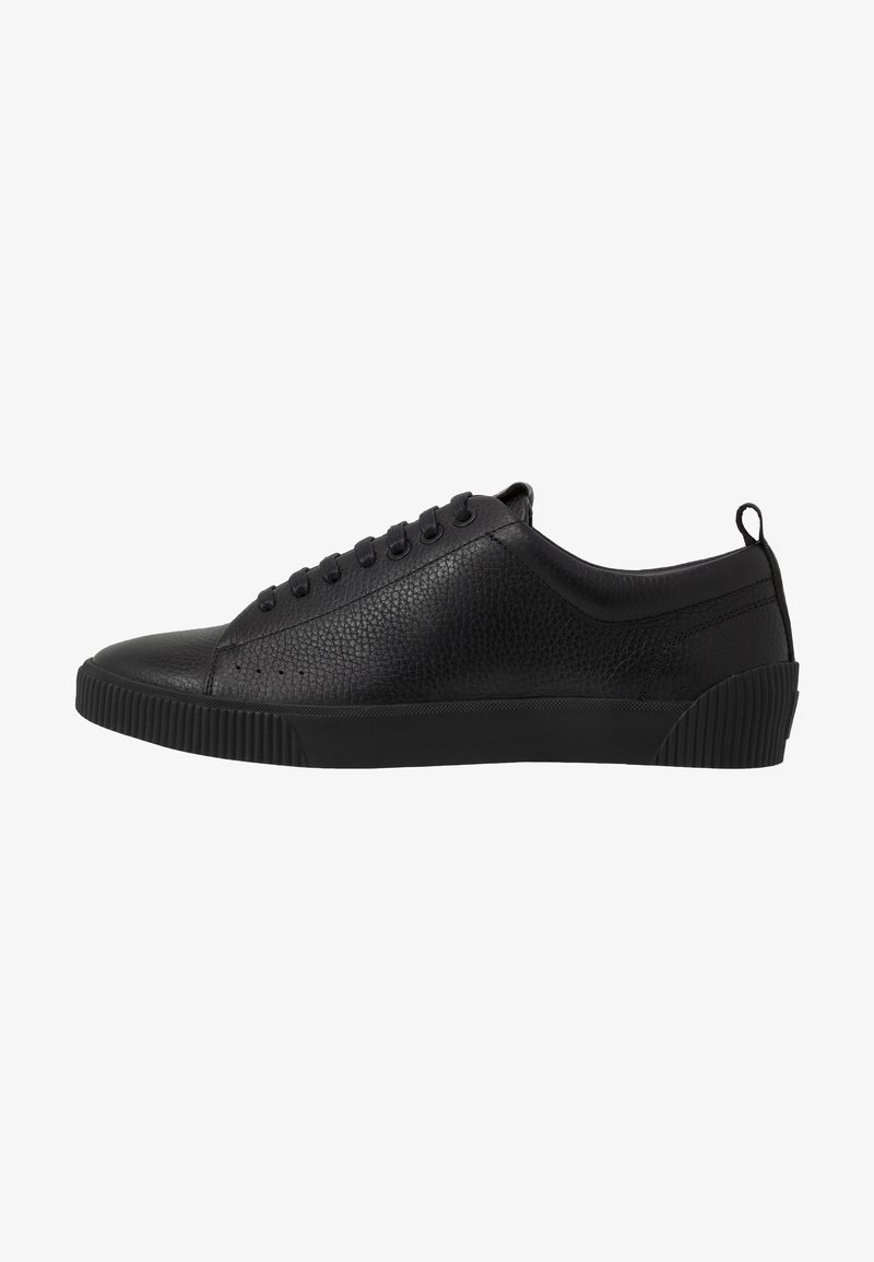 Baskets basses en cuir noir avec surface texturée, lacets noirs, semelle en caoutchouc et tirant au talon, vues de profil.