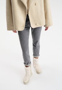 Beige shearling-takki, harmaat kapeat farkut ja valkoiset karvavuorella varustetut tennarit, joissa on tekstuuriset yksityiskohdat ja nauhat, esittelevät rentoa talvilookia.
