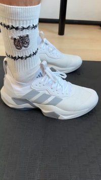 Witte sportschoenen met grijze accenten, een gestructureerd mesh bovenwerk en veters. Draagt witte geribbelde sokken met een zwart design.