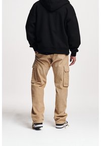 Czarny hoodie o luźnym kroju, zestawiony z beżowymi spodniami cargo z korduroy z dwoma bocznymi kieszeniami. Czarno-białe sneakersy.