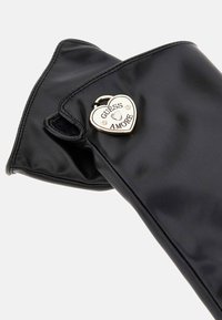 Borsa a tracolla in ecopelle nera con un charm a forma di cuore dorato inciso con "GUESS AMORE" e arricchito con strass. Superficie liscia.