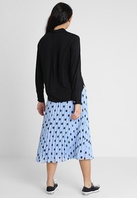 Haut noir à manches longues associé à une jupe plissée bleu clair à pois noirs, porté avec des baskets noires.