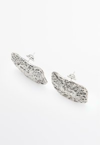 Silver-toned metal earrings with an organic, textured shape, featuring a slightly irregular outline and a polished surface.