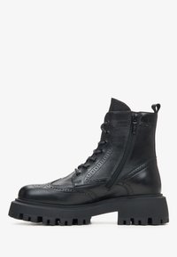 Black leather ankle boot with brogue detailing, side zipper, lace-up front, and thick lug sole for extra grip and durability.