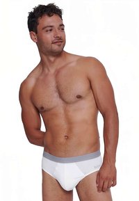 Shirtless man with short curly hair wearing white briefs with a gray waistband, looking slightly to his left against a white background.