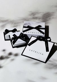 Three white gift boxes with black ribbons, featuring the brand name "LATELITA" in black lettering, arranged on a light surface.