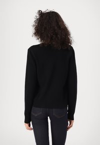 Černý pletený svetr s kulatým výstřihem, žebrovaným lemem a dlouhými rukávy. Nosený s tmavými džíny, pohled zezadu.