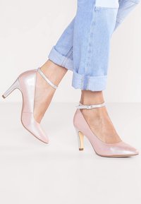 Scarpe con tacco alto in pelle verniciata rosa, con cinturini alla caviglia argentati e un tacco con dettagli dorati. Texture liscia e design a punta.