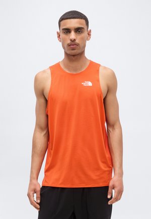 Mann iført en oransje ermeløs treningsgenser med The North Face-logo, stående mot en ensfarget lys grå bakgrunn.