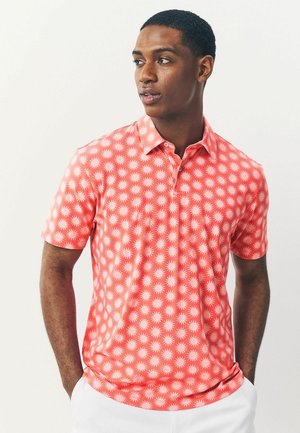Polo de manga corta en color coral, con un patrón de rayo de sol. Fabricado en una tela suave con un cuello clásico y una tapeta de tres botones.