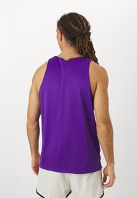 Lila ujjatlan sporttop légáteresztő hálós anyagból, laza fazonnal és oldalsó hasítékokkal a nagyobb mozgásszabadság érdekében.