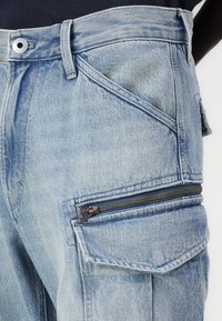 Ανοιχτό μπλε τζιν Cargo παντελόνι με πολλά τσέπες, τσέπη με φερμουάρ στο πλάι και ίσια γραμμή. Διαθέτει κούμπωμα με κουμπί και θηλάκια για ζώνη.