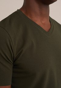 Camiseta verde oliva de cuello en V hecha de suave tejido de algodón. Presenta mangas cortas, un corte ajustado y costuras limpias a lo largo del escote.
