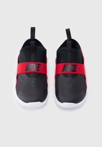 Baskets à enfiler Nike en noir et blanc avec des bandes élastiques rouges sur le dessus, arborant des logos Nike noirs et des languettes pour tirer au niveau du talon.