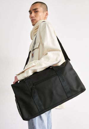 Črn vodoodporen nahrbtnik z žepom na zadrgo, opremljen z nastavljivimi trakovi in mrežnim stranskim vložkom; eleganten dizajn in minimalistično označevanje.