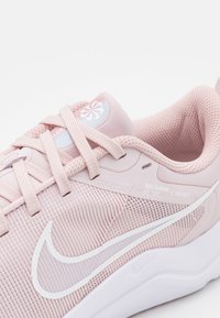 Zapatilla de running Nike rosa con parte superior de malla, tejido texturizado, logo Swoosh blanco y un collar acolchado. Presenta cordones planos y detalles de marca.