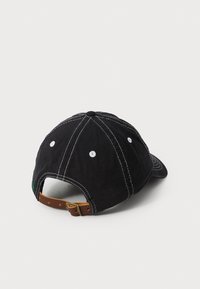 Casquette noire en coton avec des coutures blanches, sangle en cuir marron ajustable, et une aération ronde à l'arrière.