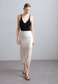 Črn rebrast bodysuit z globokim izrezom, v kombinaciji s prosojno, dolžino do kolen belo krilo. Model nosi črne sandale z narami.
