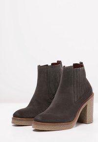 Harmaat mokkasaappaat nilkkoihin, joissa on joustavat sivupaneelit, karkeapintainen beige alustapohja ja sileä pyöreä kärki. Saumadetaillointi sivuilla.