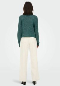 Pull en maille côtelée teal à manches longues, associé à un pantalon blanc large et des bottines noires. Vue de dos.