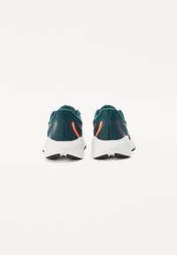 Sneakers in mesh turchese con suole bianche, caratterizzate da dettagli neri e arancioni vivaci. Tacco arrotondato e superficie strutturata.