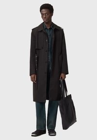 Cappotto nero a doppio petto con chiusura a bottoni e spalline, abbinato a jeans scuri e borsa a tracolla nera.