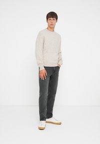Lys beige strikket sweater, afslappet pasform; mørke grå jeans; hvide sneakers med brune såler. Enkel, struktureret design, minimal accents.