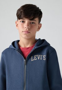 Felpa con zip di colore blu navy realizzata in tessuto morbido, dotata di zip frontale, cappuccio con cordino e logo "LEVI'S" beige sul petto.