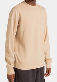 Sweat-shirt beige avec un col rond, des manches longues, et un petit logo sur la poitrine. Confectionné en tissu doux à la texture lisse.